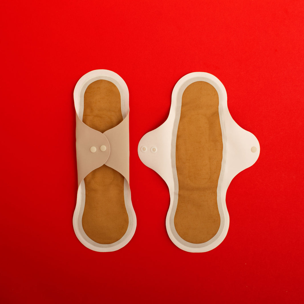 Pair of beige reusable menstrual pads with copper ion odour control top layer and SILVADUR absorbent layer with wings, on a red background