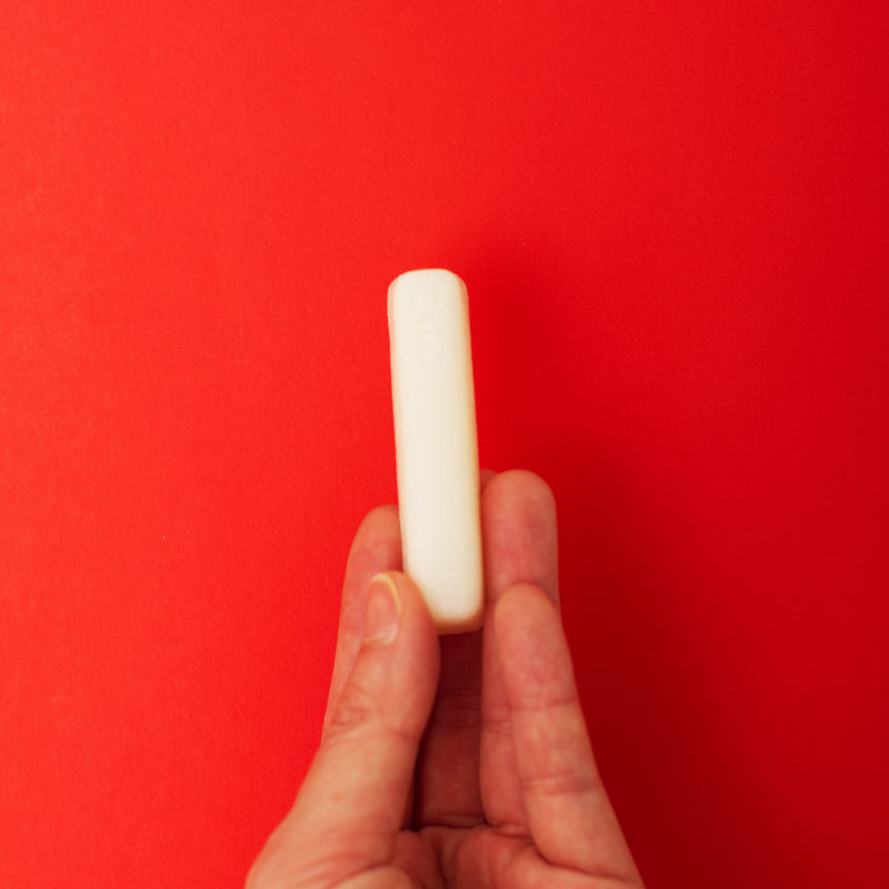 Hand holding a white stain remover stick for menstrual care and reusable menstrual products against a red background