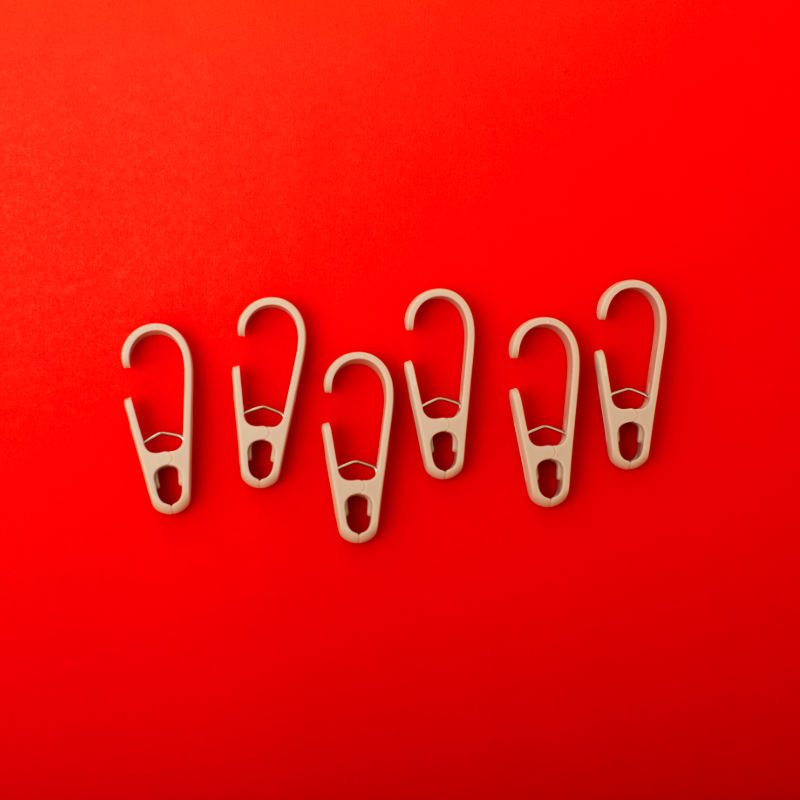 Six beige clothing clip hooks on a red background