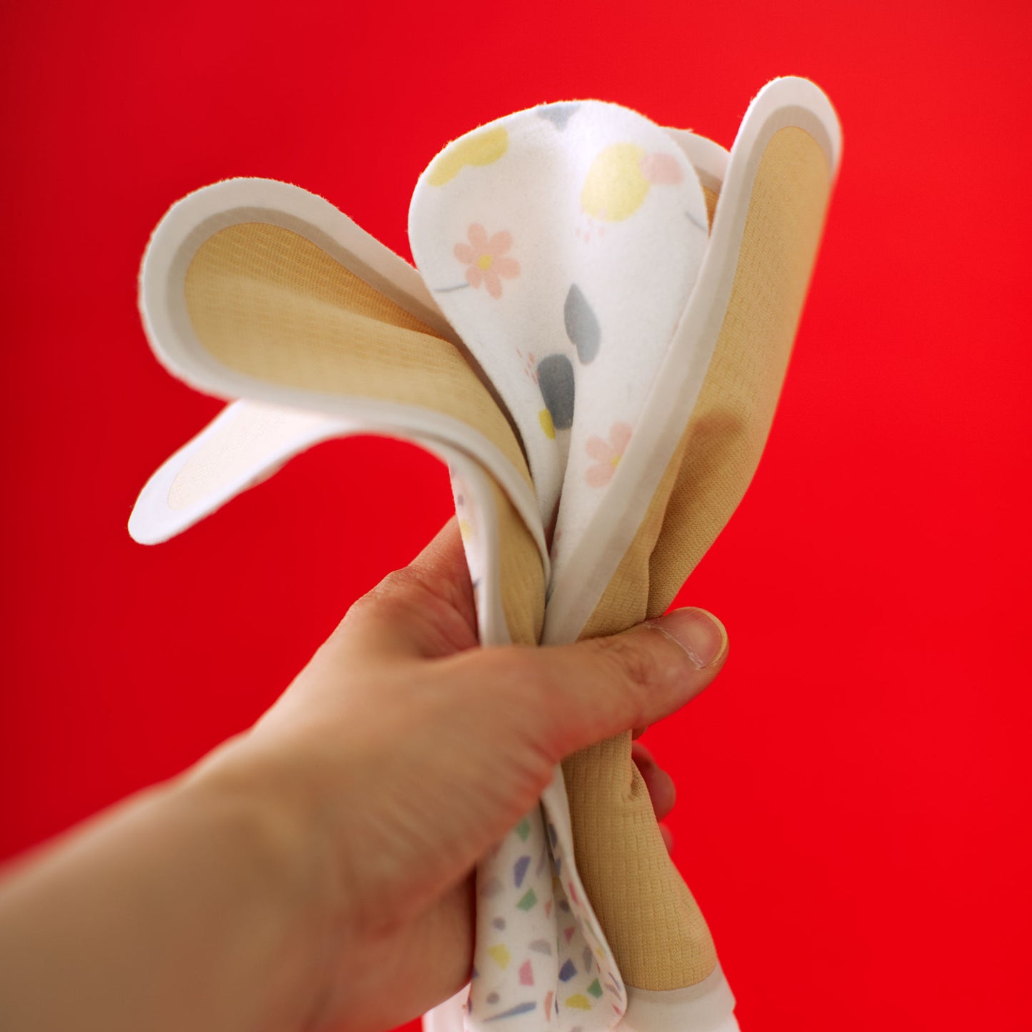 Hand holding a bundle of ultra thin reusable panty liner with colorful patterns against a red background