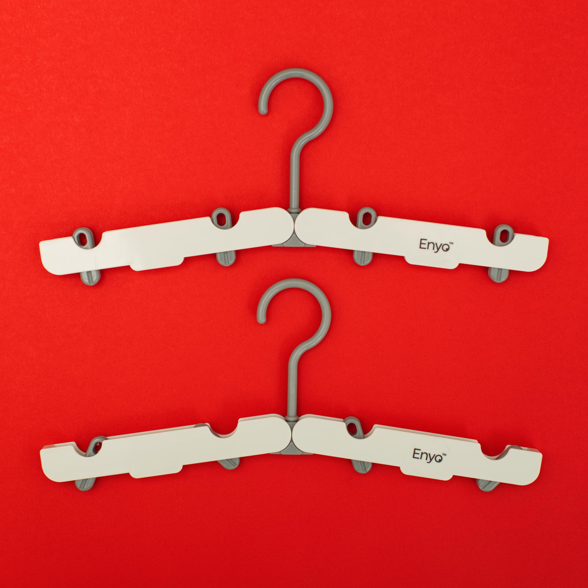 Two white and light grey plastic foldable hangers with 4 clips on a red background
