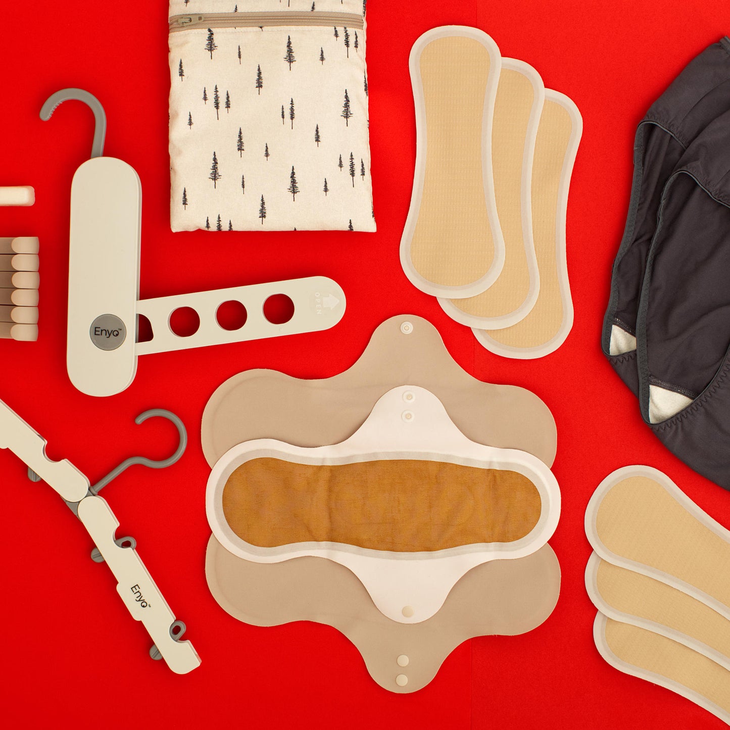 Various menstrual care products including foldable hangers and reusable period pad, panty liners and black underwear, wet dry bag, foldable hanger rack, and hook clips on a red background.