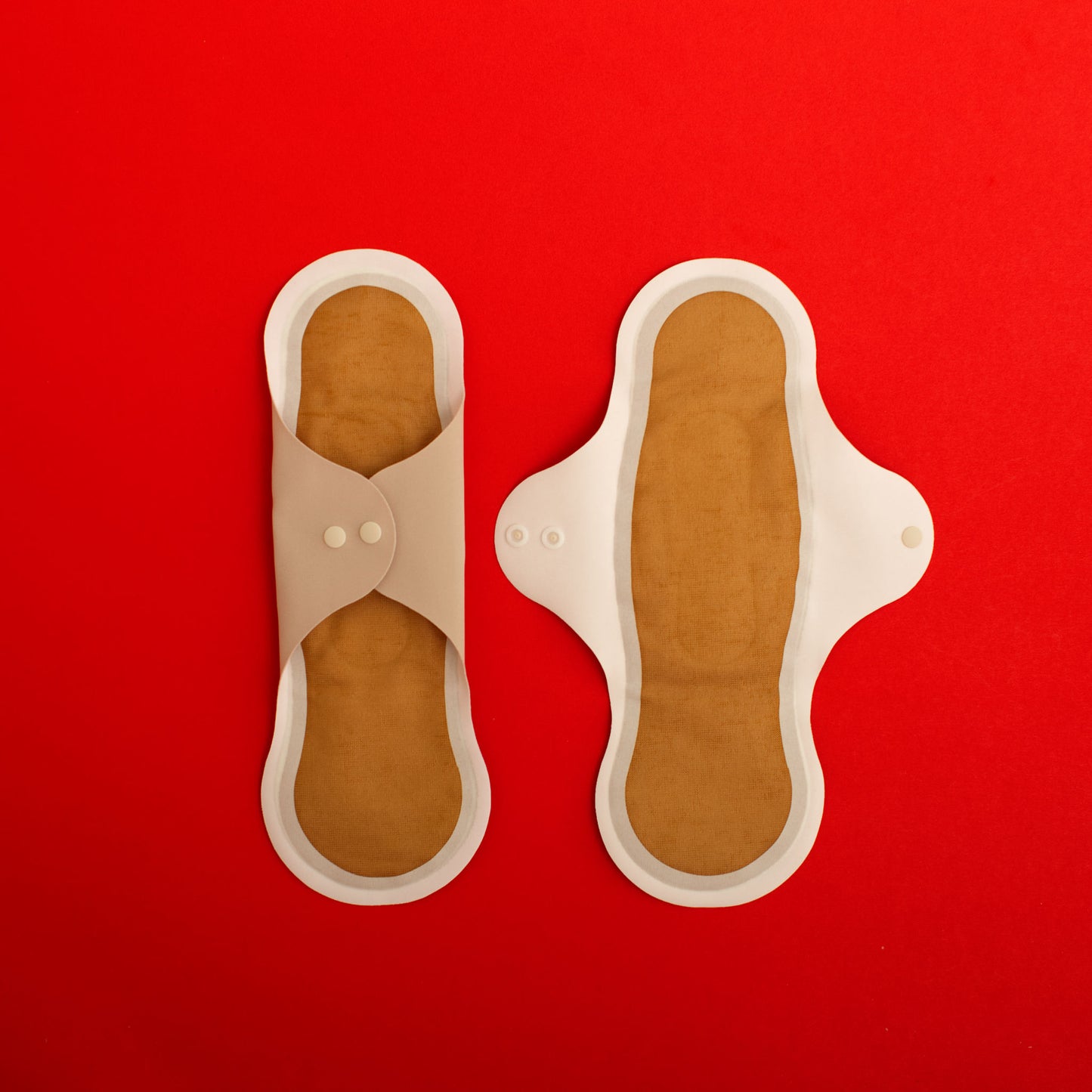 Pair of beige reusable menstrual pads with copper ion odour control top layer and SILVADUR absorbent layer with wings, on a red background