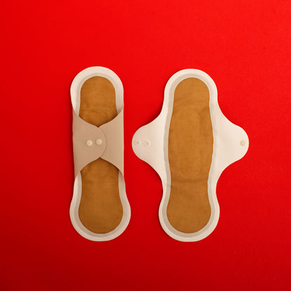 Pair of beige reusable menstrual pads with copper ion odour control top layer and SILVADUR absorbent layer with wings, on a red background