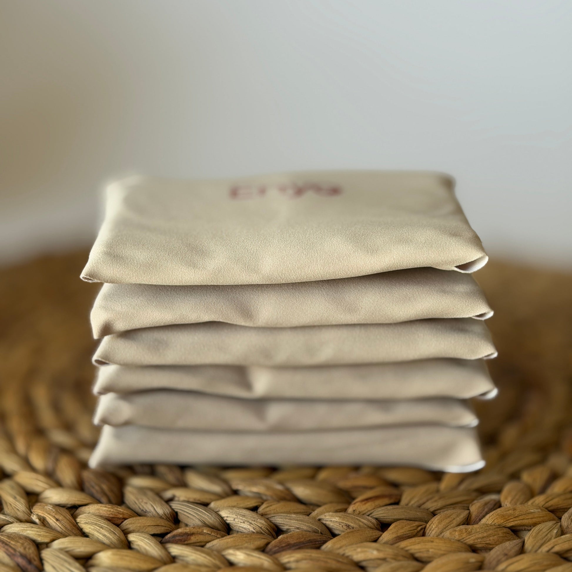 Stack of beige reusable menstrual cloth pads folded on a natural placemat